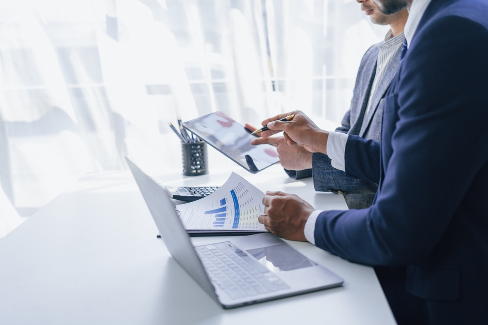 Two business people side-by-side in a light and airy conference room, looking over charts and data.